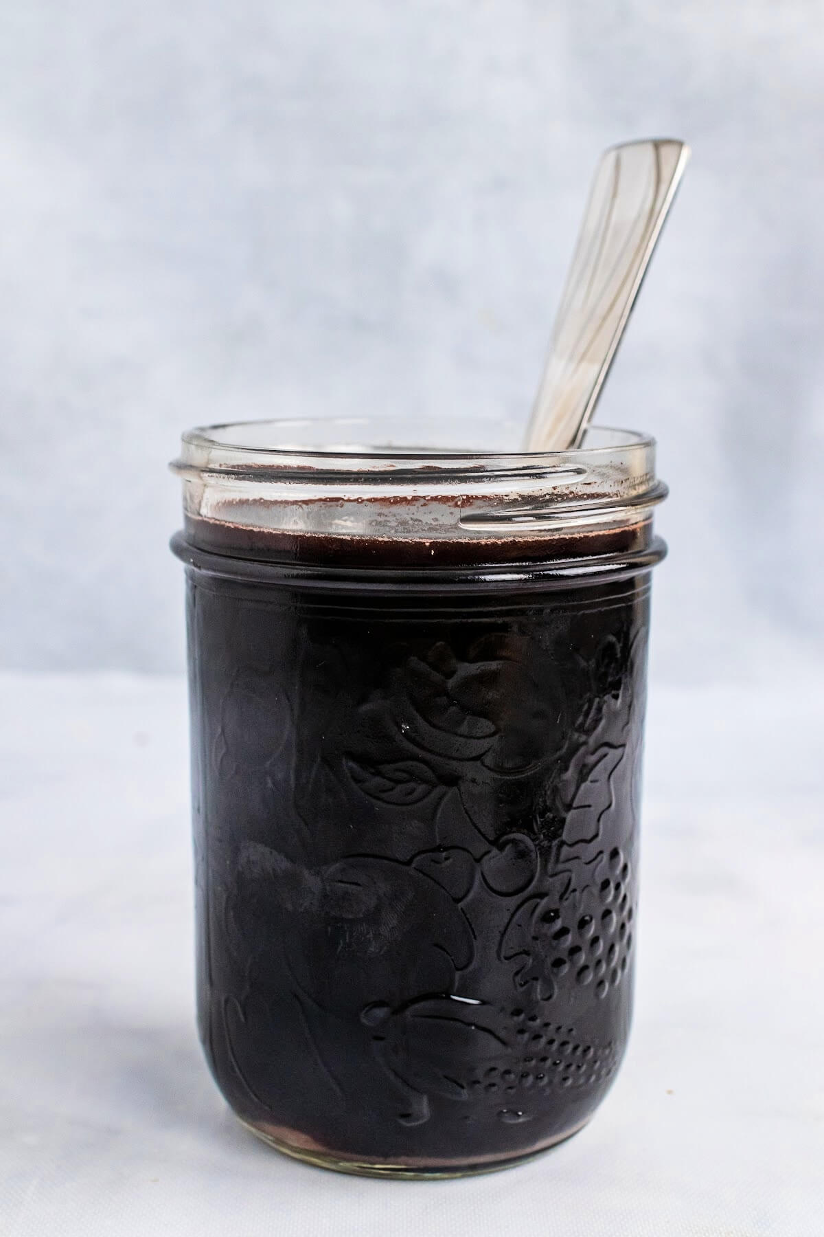 Mason jar full of dark purple syrup with a spoon sitting in the jar.