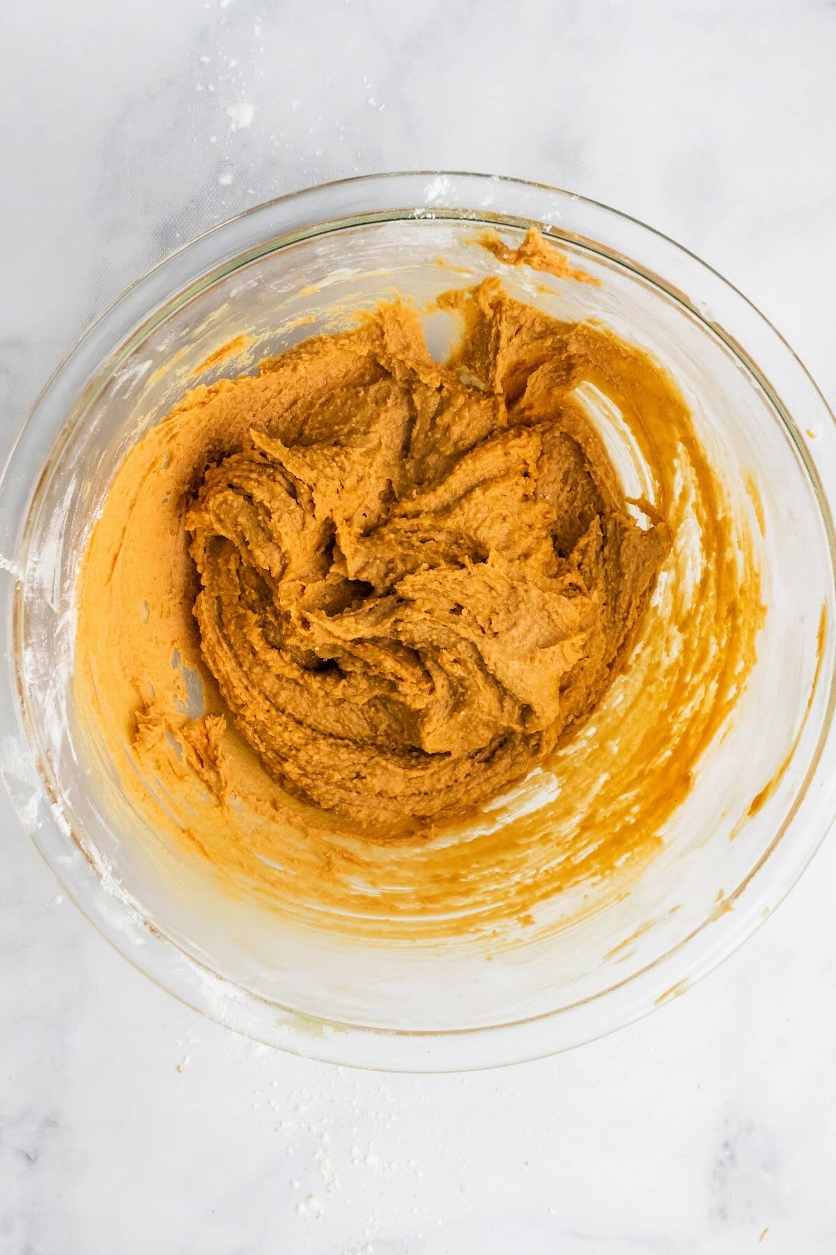 A glass mixing bowl filled with a creamy, thick peanut butter mixture.