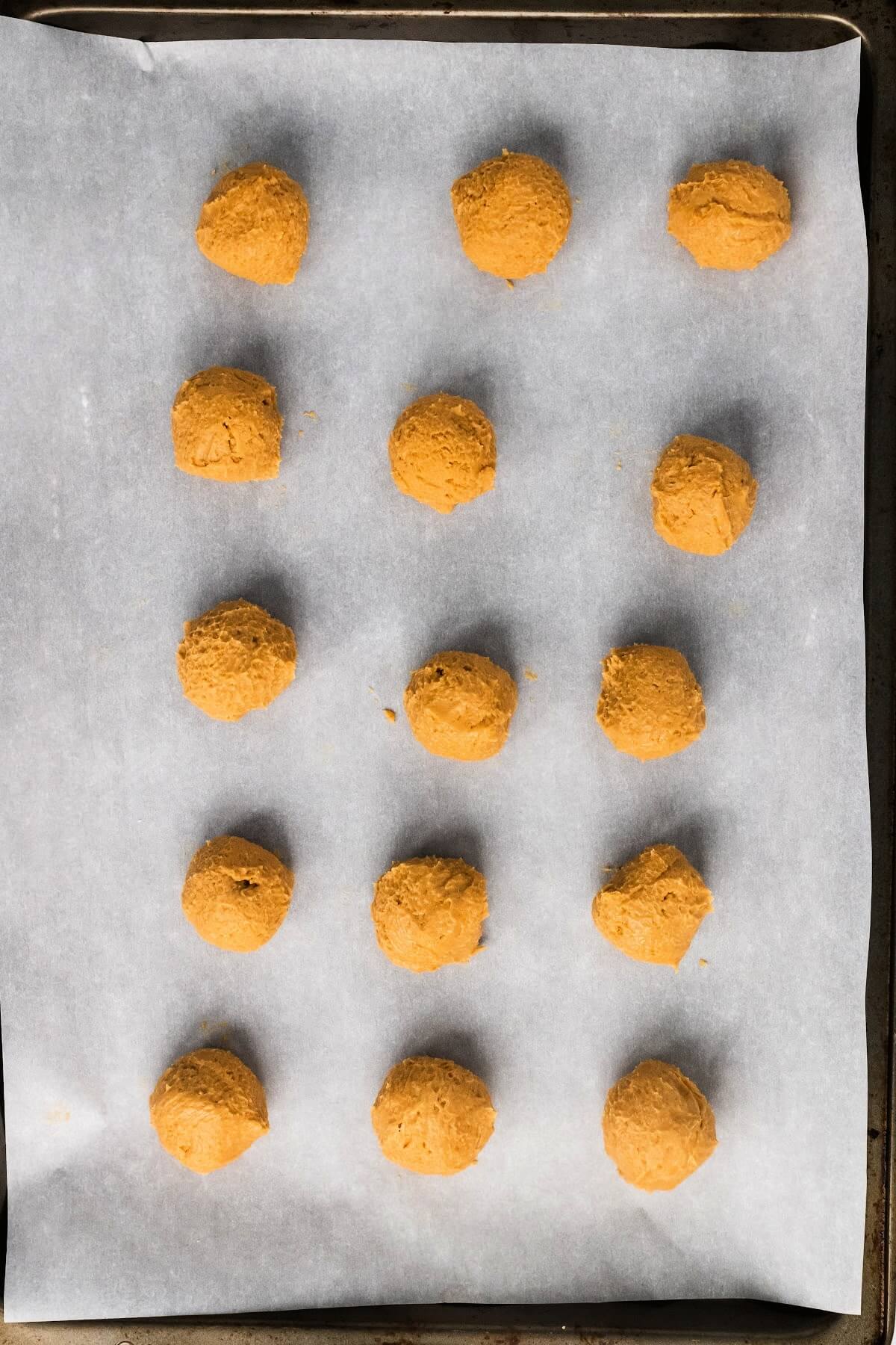 A baking sheet lined with parchment paper with 15 rolled balls of peanut butter truffles.