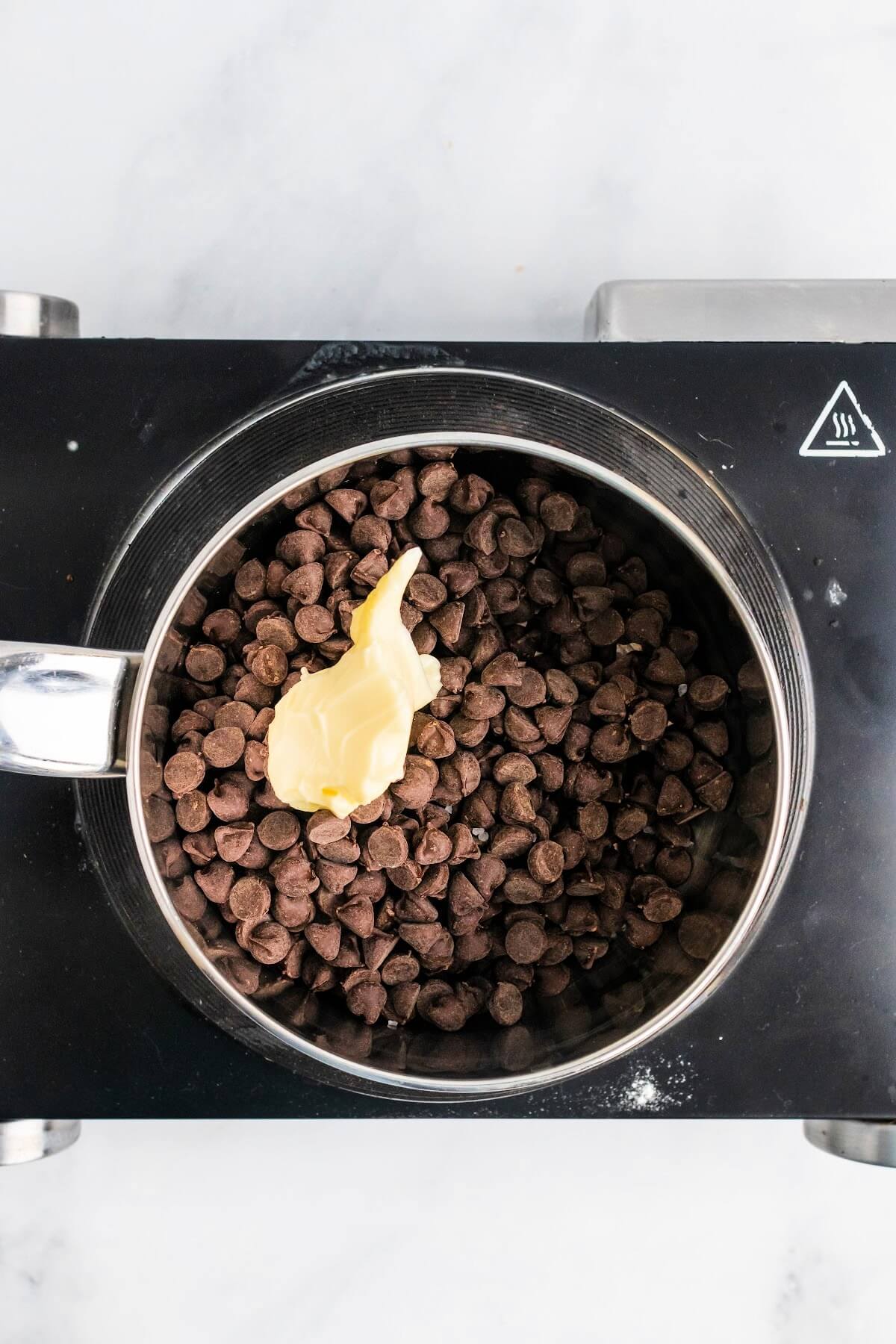 A saucepan filled with chocolate chips and a spoonful of butter sitting on top of an electric stovetop.