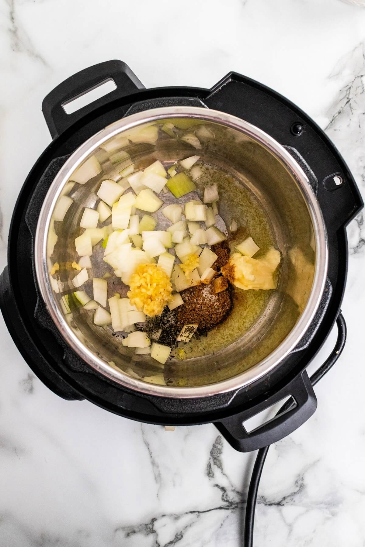 Overhead shot of an Instant Pot with melting butter, spices, fresh crushed garlic and chopped of onions.