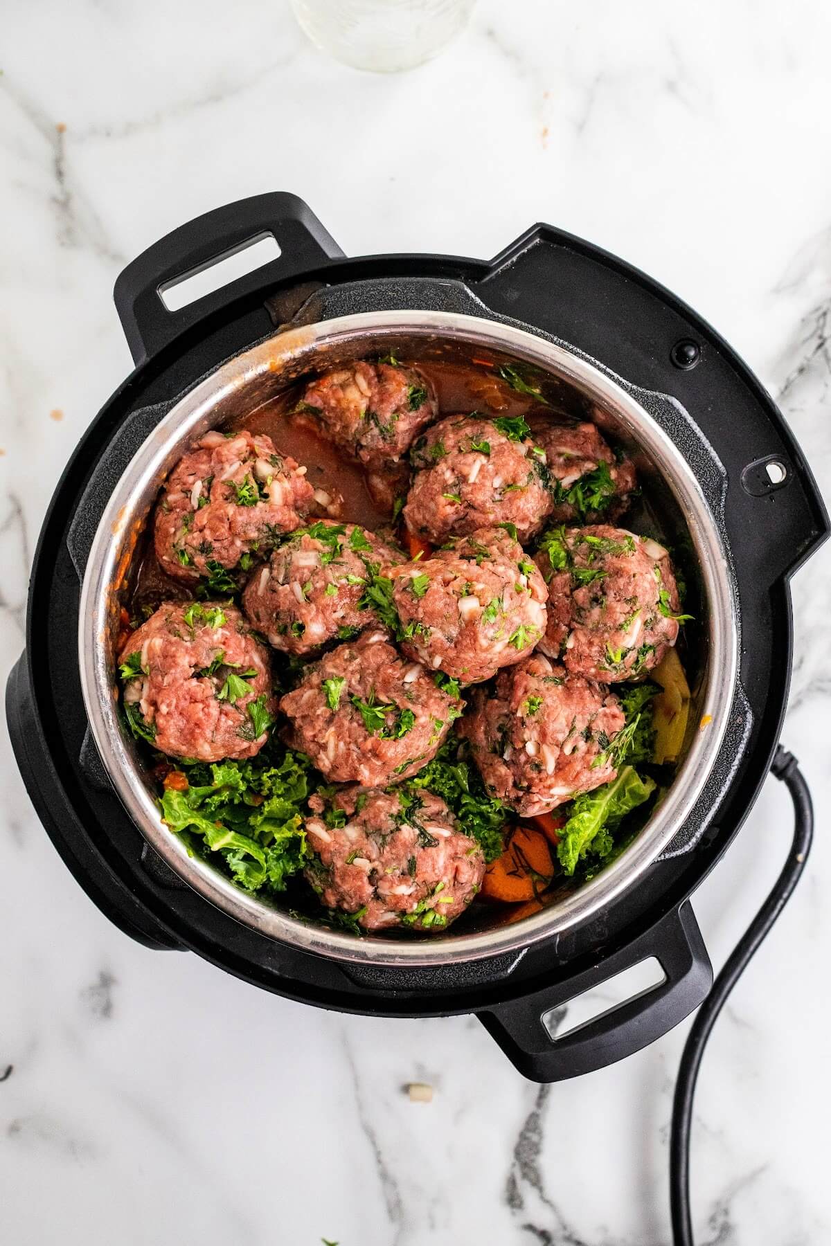Overhead shot of an Instant Pot filled with meatballs with fresh greens sitting on top of vegetables and broth.