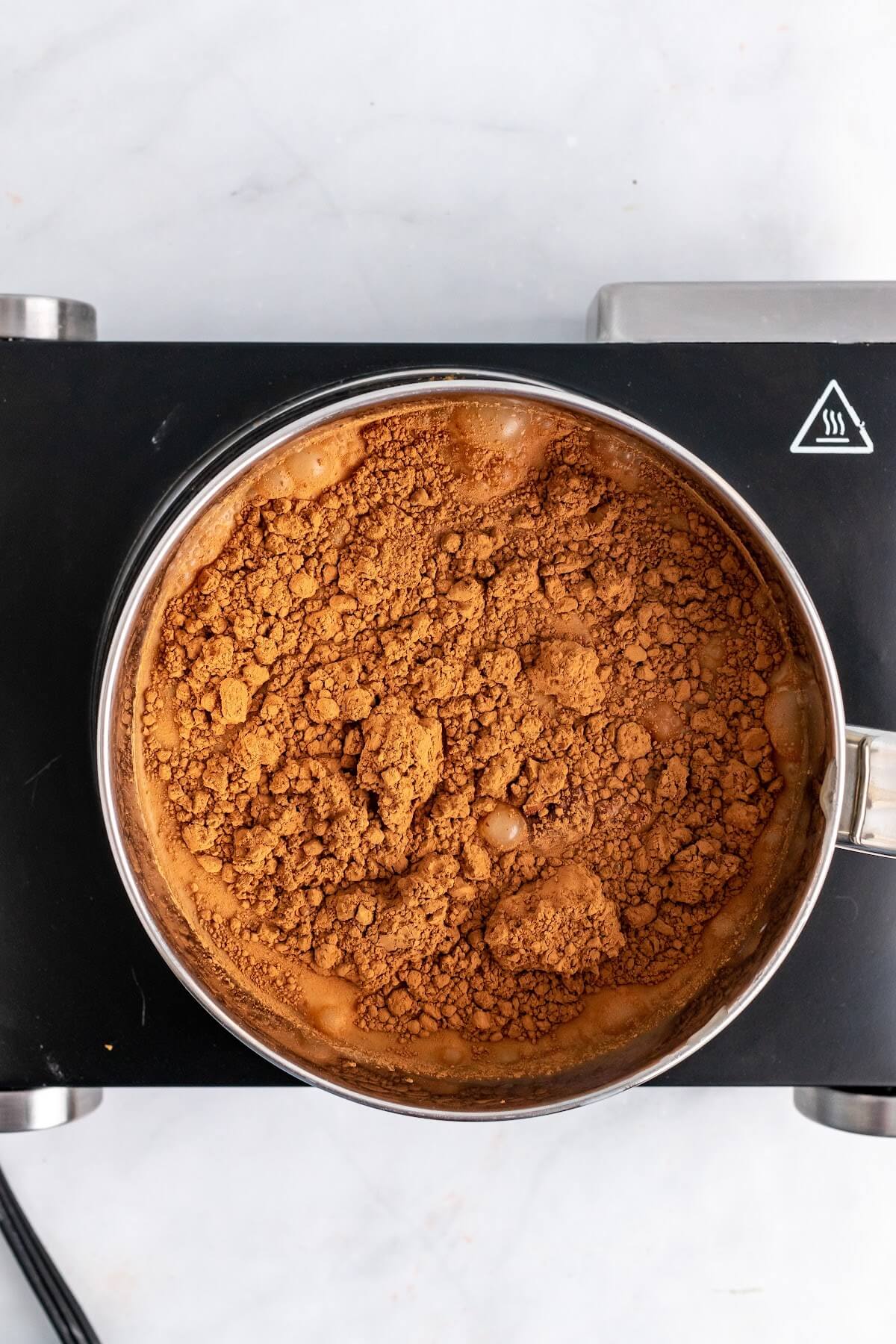 Saucepan filled with liquid and cocoa powder covering the liquid sitting on top of a stovetop.