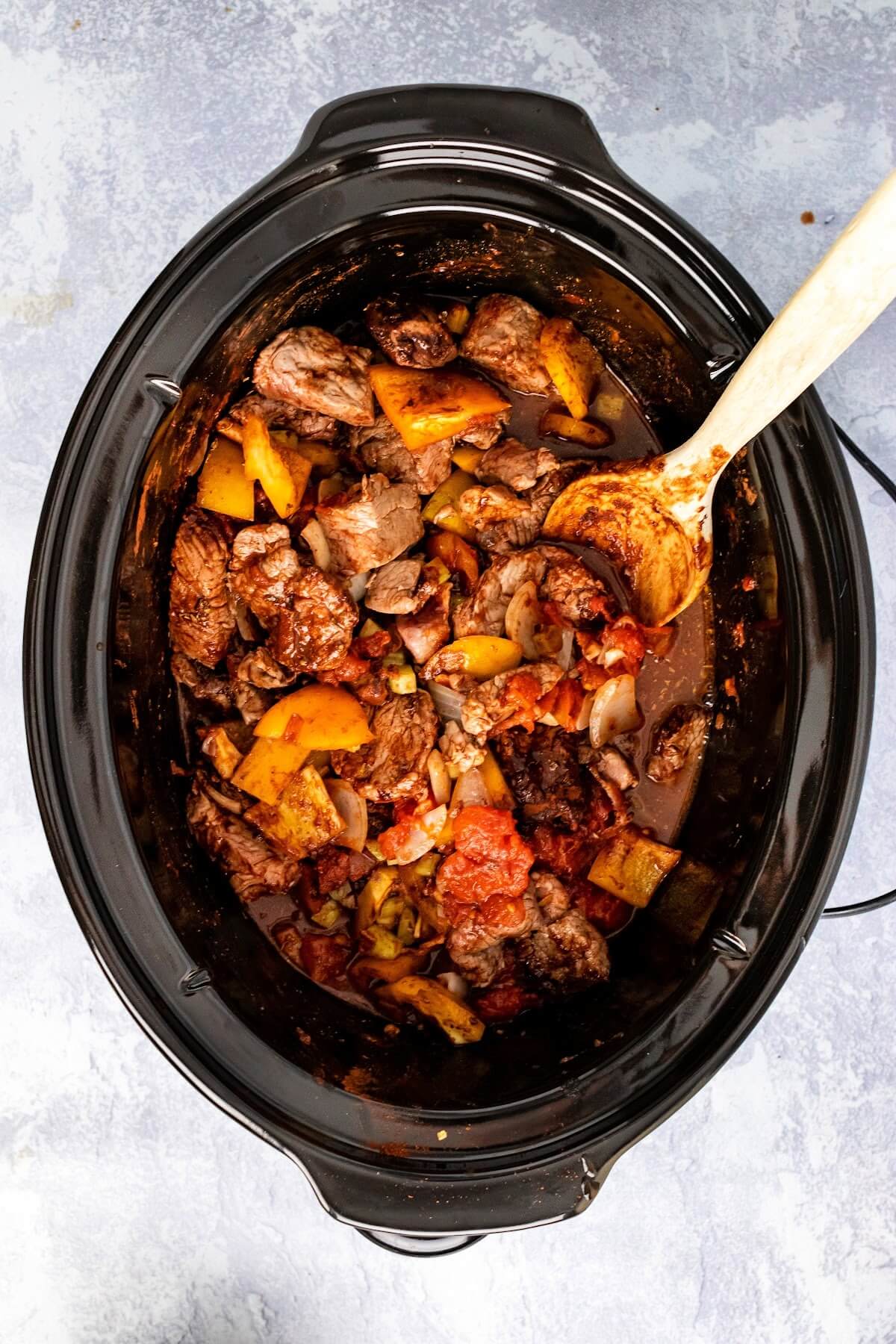 Slow cooker with uncooked chili ingredients that have been stirred together with a mixing spoon.