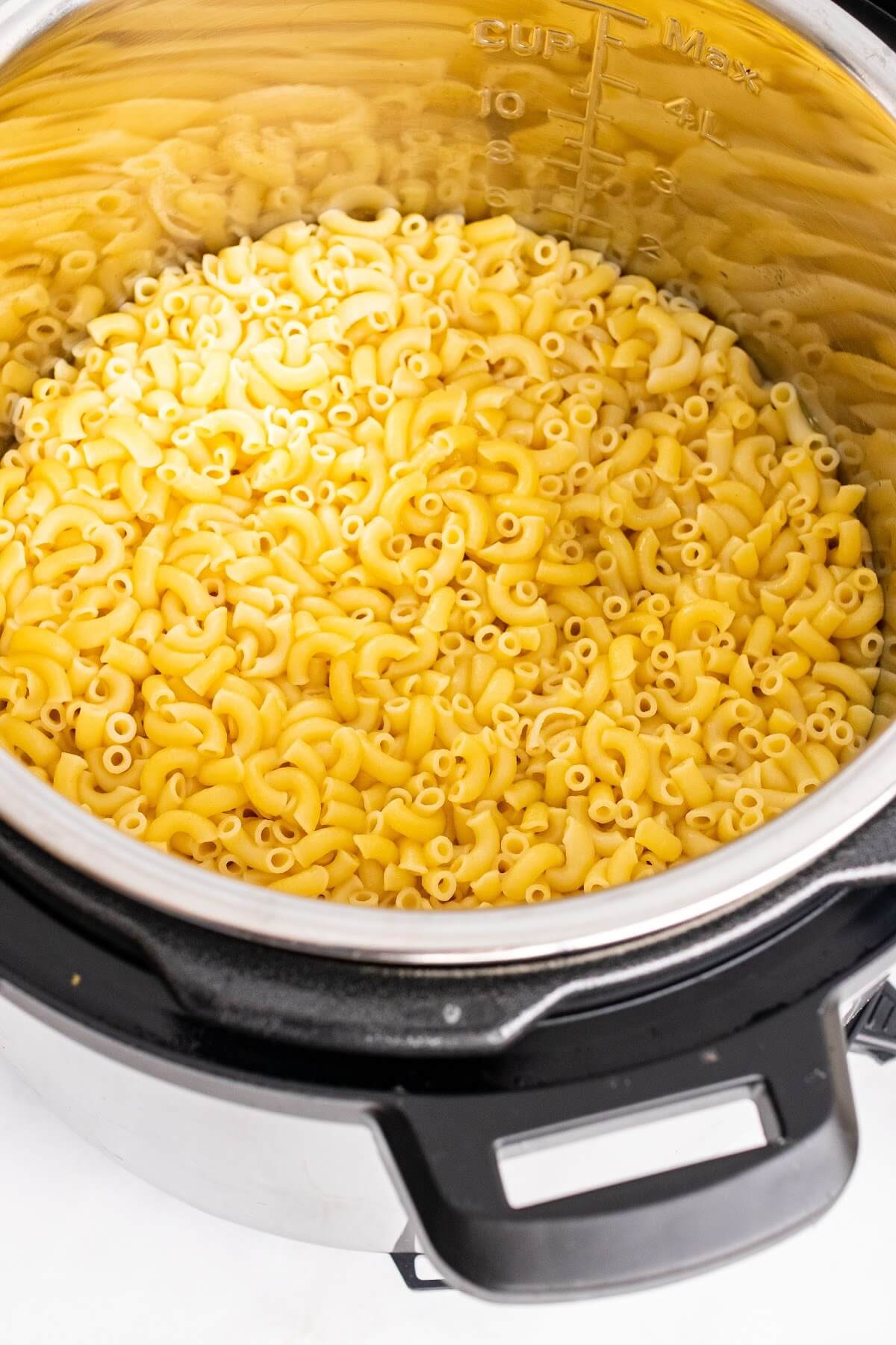 An Instant Pot half full of dry macaroni pasta.