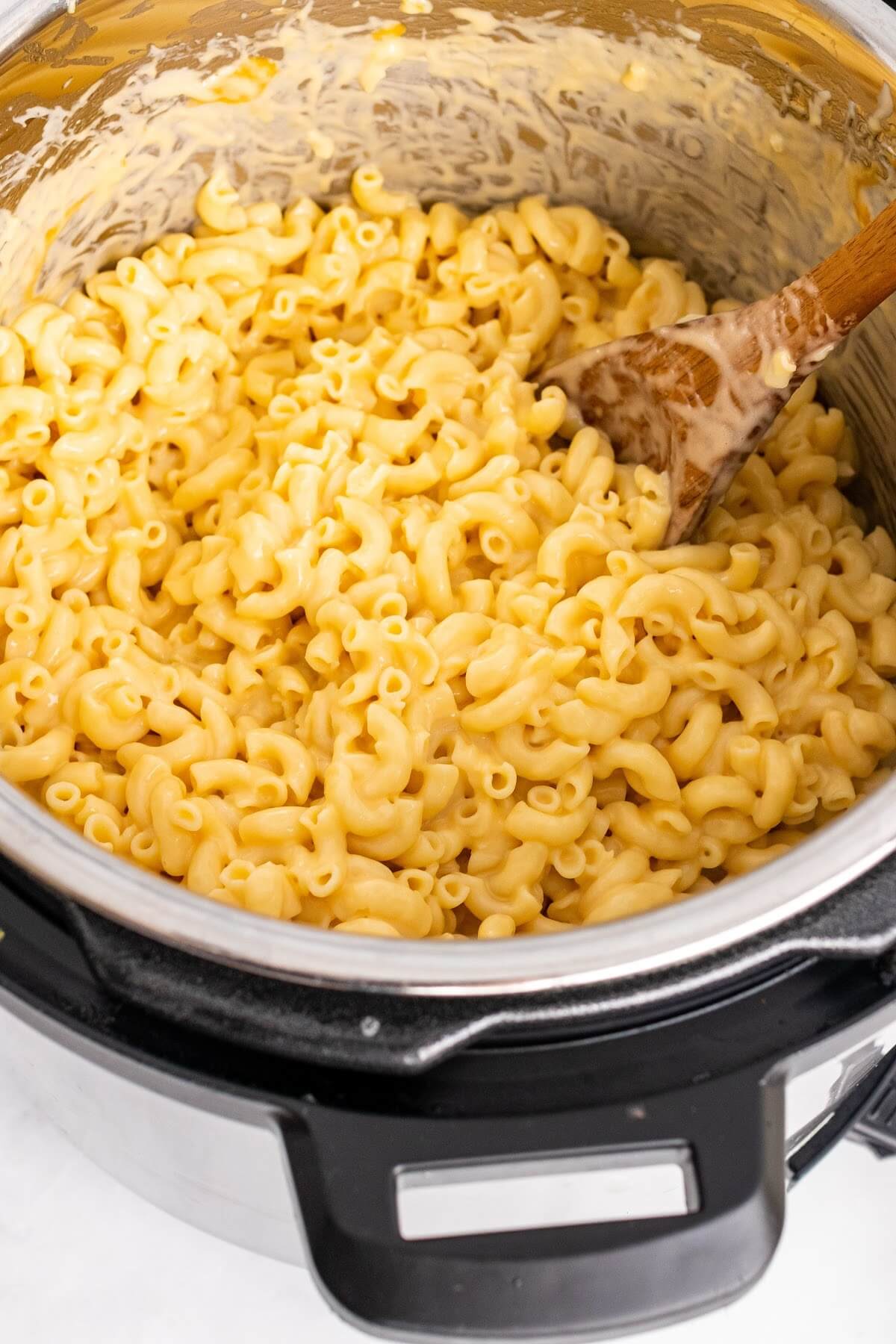 An Instant Pot filled with cooked macaroni and cheese being stirred by a wooden spoon.