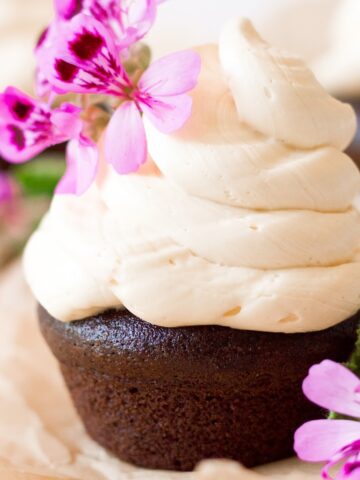 Chocolate cupcake topped with a 2-inch swirl of vanilla buttercream frosting and pink geranium flowers for garnish.