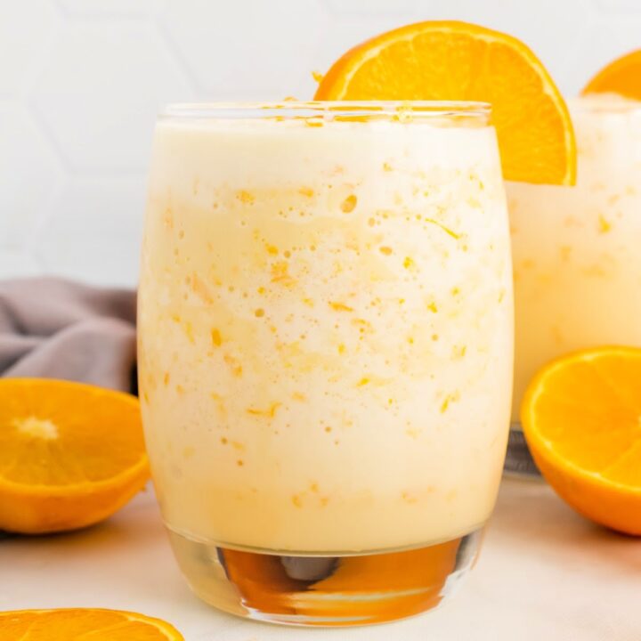 Creamy orange smoothie in a two glasses with fresh orange slices and whole oranges slices in the background.