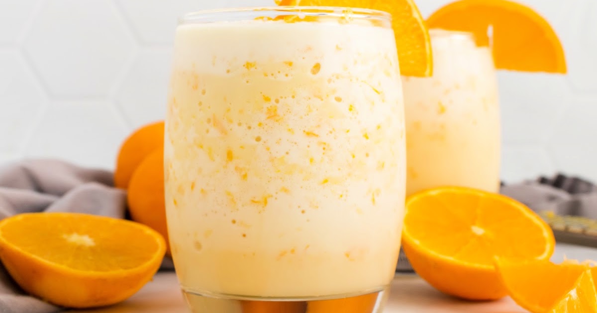 Creamy orange smoothie in a two glasses with fresh orange slices and whole oranges slices in the background.
