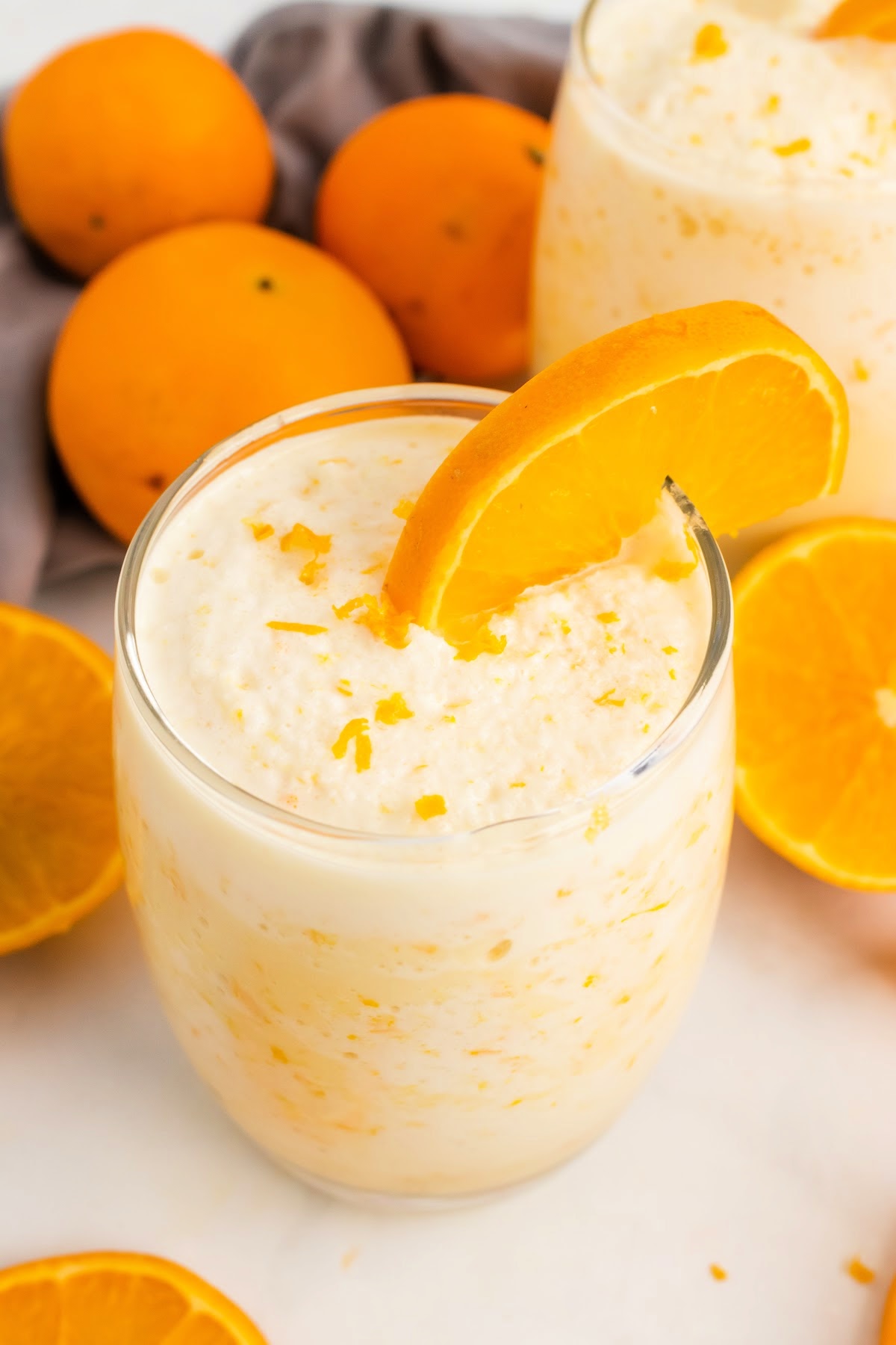 Creamy orange smoothie in a two glasses with fresh orange slices and whole oranges sitting in the background.