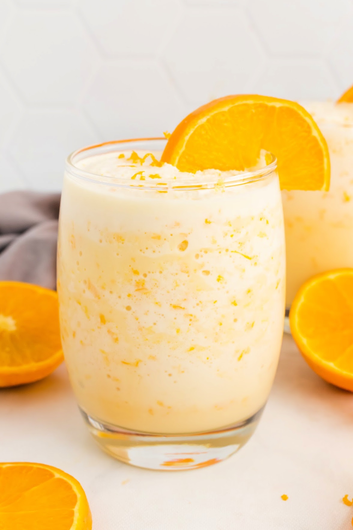 Creamy orange smoothie in a glass with fresh orange slices and oranges sitting around the glass.