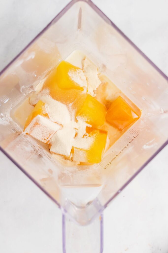 Frozen orange juice ice cubes, milk and other ingredients inside a blender.