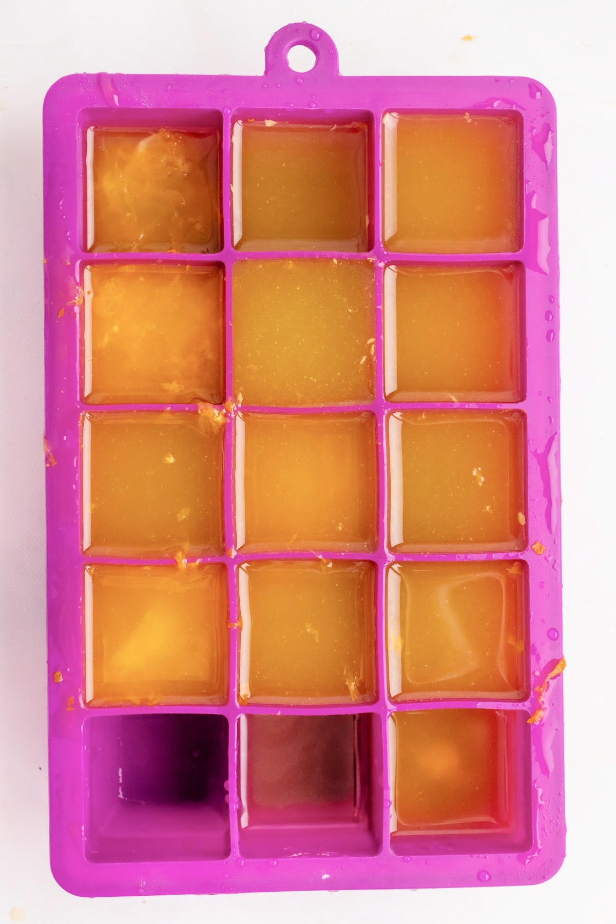 Frozen orange juice ice cubes in a pink silicone ice cube tray.