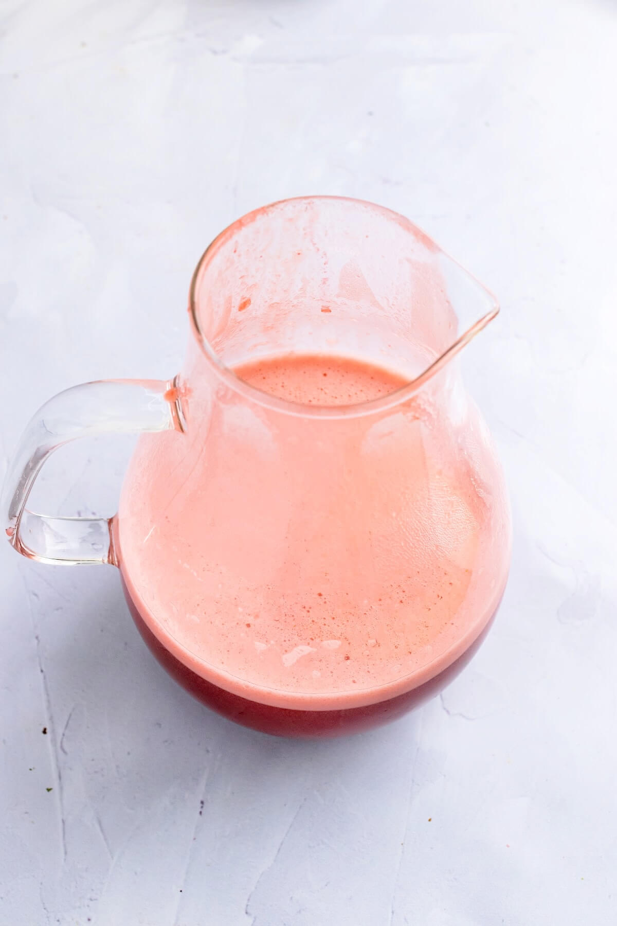 An overhead view of a glass pitcher half filled with a frothy red liquid, sitting on top of a marble surface.